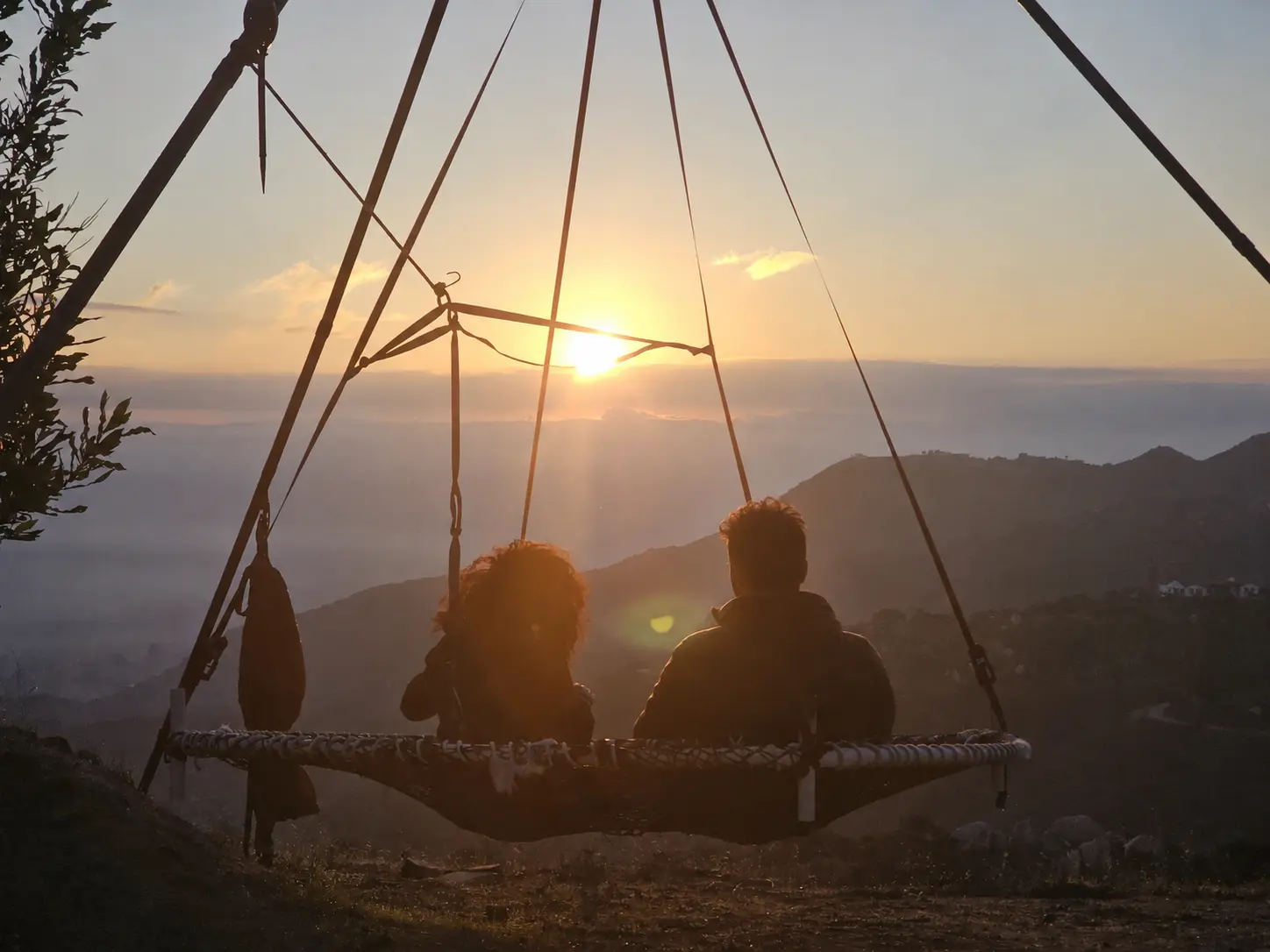 Two people on the suspended circular bed at sunrise, the Wildomar hills in gold below